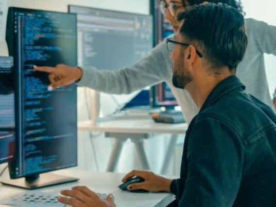 Mitarbeitende schauen auf Code auf einem Bildschirm. Mitarbeitende schauen auf Code auf einem Bildschirm.