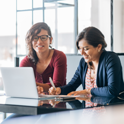 Zwei Frauen am Schreibtisch. Zwei Frauen arbeiten an einem Schreibtisch mit einem Laptop vor ihnen.